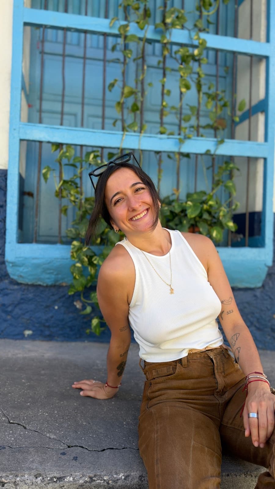 Natalia Vital sonriendo, sentada frente a una ventana azul con plantas